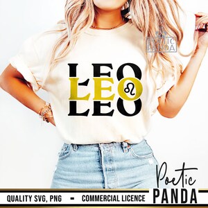 May include: A white t-shirt with a black and gold graphic design that says "LEO" three times with the Leo zodiac symbol in the middle. The shirt is being worn by a person with long blonde hair and blue jeans.