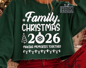 Può includere: Una felpa corta verde scuro con la scritta bianca Family CHRISTMAS 2026 MAKING MEMORIES TOGETHER. Il design include la grafica di un albero di Natale, una pallina decorata con un fiocco di neve e una fila di luci pendenti.