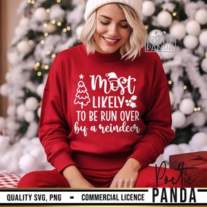 May include: A red sweatshirt with the text "Most Likely To Be Run Over by a Reindeer" in white. The sweatshirt features a Christmas tree and Santa hat graphic. The person is wearing a white beanie and red pants.