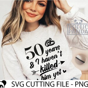 May include: A white sweatshirt with black text that reads "50 years & I haven't killed him yet" with a heart and arrow graphic. The text is in a handwritten font.
