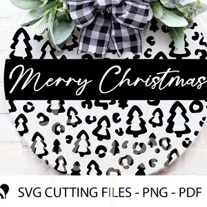 May include: Black and white round sign with a leopard print pattern and small Christmas tree silhouettes. The sign has a black banner across the middle with the text "Merry Christmas" in white.