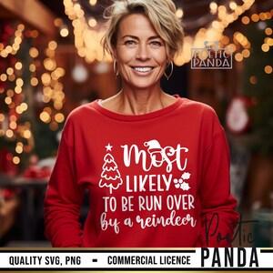 May include: A red sweatshirt with the text "Most Likely To Be Run Over By A Reindeer" in white. The design includes a Christmas tree, Santa hat, and holly. The sweatshirt is worn by a person smiling.