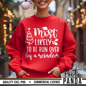 May include: A red sweatshirt with the text "Most Likely To Be Run Over by a Reindeer" in white. The design includes a Christmas tree, a Santa hat, and holly. The sweatshirt is a festive holiday apparel item.