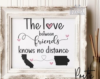 May include: A white framed print with the text "The love between friends knows no distance" and two black silhouettes of states connected by a dotted line. The print has a pink heart and pink hearts along the dotted line.