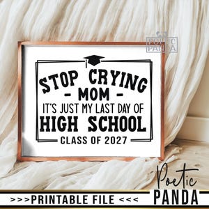 May include: A rectangular sign with a copper-colored frame featuring black text on a white background that reads: STOP CRYING MOM IT'S JUST MY LAST DAY OF HIGH SCHOOL CLASS OF 2027, topped with a black graduation cap icon and double-line borders.