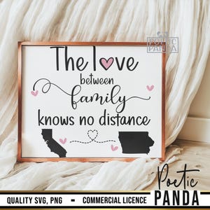 May include: A white wooden sign with a brown frame, featuring the text "The love between family knows no distance". The sign has a pink heart and two pink hearts on either side of the text. The sign also has two black outlines of states, one on each side of the text, connected by a dashed line with a pink heart in the middle.