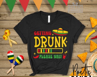Può includere: Maglietta nera con una grafica di un sombrero e il testo "Getting Drunk + Please Wait". La grafica include una barra di avanzamento con strisce verdi, rosse e gialle.