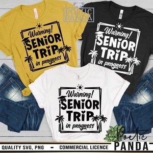 May include: Three t-shirts with a black and white graphic design that says "Warning! Senior Trip in progress". The graphic includes a graduation cap, a heart, palm trees, and a sun. The t-shirts are on a wooden surface with a pair of blue jeans.