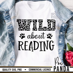 Puede incluir: Camiseta blanca con las palabras "WILD about READING" en letras negras. La palabra "WILD" tiene un estampado de jirafa en blanco y negro. Dos huellas de patas negras est&aacute;n debajo de las palabras "WILD about". La camiseta se muestra sobre una chaqueta vaquera.
