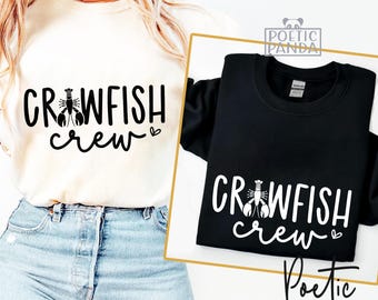 May include: Two sweatshirts, one cream and one black, each with the words "CRAWFISH crew" in a bold, stylized font. A crawfish graphic is centered above the word "crew". The cream sweatshirt is being worn. The black sweatshirt is displayed on a gold-edged card.