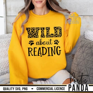 Puede incluir: Sudadera amarilla mostaza con el texto negro "WILD about READING". La palabra "WILD" tiene un estampado de jirafa. Huellas de patas a ambos lados de la palabra "about". La sudadera es de cuello redondo y manga larga.