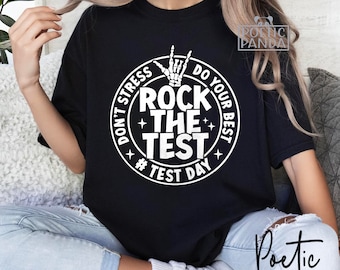 Puede incluir: Camiseta negra con un gráfico circular blanco que dice "Don't Stress Do Your Best Rock The Test #Test Day". El gráfico también incluye una mano de esqueleto haciendo el gesto de rock and roll.