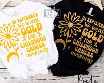 Puede incluir: Una camiseta blanca y una negra, ambas con un gráfico de margarita amarilla y el texto: IN SEPTEMBER WE WEAR GOLD FOR CHILDHOOD CANCER AWARENESS. La camiseta negra muestra el diseño en textura de purpurina dorada, mientras que la blanca usa amarillo.