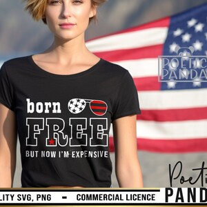 May include: Black t-shirt with white text that reads "born FREE BUT NOW I'M EXPENSIVE". The text is surrounded by a red, white, and blue graphic of sunglasses. The t-shirt is worn by a person standing in front of an American flag.