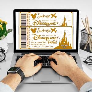 May include: A laptop displays two gold-colored Disneyland boarding passes with the text "Surprise, You're Going to Disneyland Paris!" and "Mom and Dad." The laptop is on a desk with a clock, pencils, and glasses.