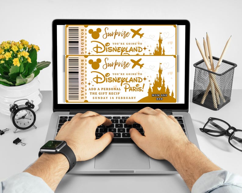 May include: A laptop displays two gold-colored Disneyland boarding passes with the text "Surprise, You're Going to Disneyland Paris!" and "Mom and Dad." The laptop is on a desk with a clock, pencils, and glasses.