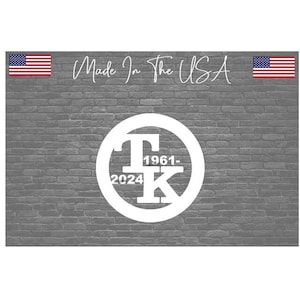 May include: White circle with the letters "T" and "K" inside, with the years "1961" and "2024" on either side of the letters. The circle is on a gray brick wall background. The text "Made in the USA" is above the circle.