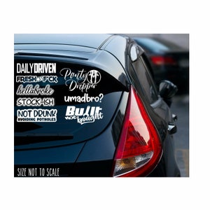 May include: A collection of white vinyl car decals with various phrases and words, including "Daily Driven," "Party Dropper," and "Built Not Bought." The decals are displayed on the rear window of a black car.