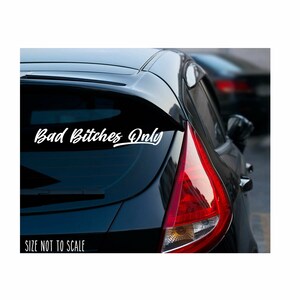 May include: A white vinyl decal with the text "Bad Bitches Only" in a cursive font, applied to the rear window of a black car. The car's taillight is red. The text "SIZE NOT TO SCALE" is below the decal.