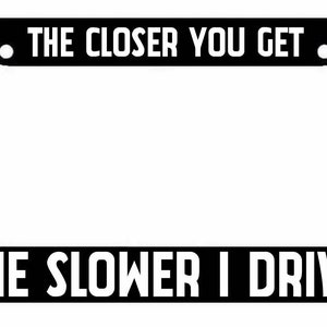 May include: Black license plate frame with white text that reads "The closer you get, the slower I drive."