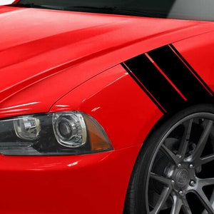 May include: Bright red car with black racing stripes on the front fender. The stripes are angled and parallel, adding a sporty look. The car's headlight and wheel are visible, showcasing a sleek design.