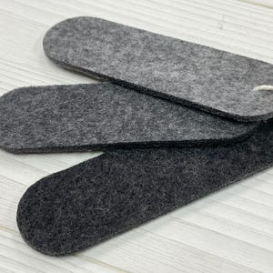 May include: Three gray felt pieces in the shape of an oval. The pieces are stacked on top of each other.