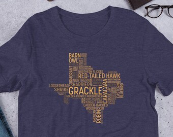 May include: A navy blue t-shirt with a gold outline of the state of Texas. The outline is filled with words related to Texas birds, including "Barn Owl", "Red-Tailed Hawk", "Grackle", and "Caracara".