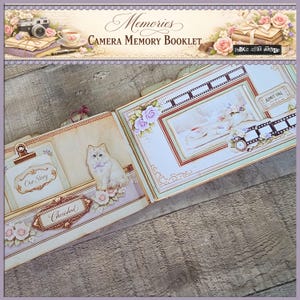 May include: Open scrapbook titled "Memories Camera Memory Booklet" with decorative pages. Features include a cat illustration, floral accents, and the words "Our Story" and "Cherished". The design incorporates vintage elements and a film strip.