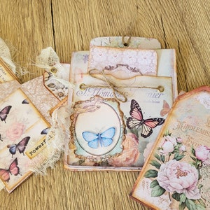 K&ouml;nnte beinhalten: Ein Satz Vintage-Scrapbook-Seiten mit floralen Designs, Schmetterlingen und Spitzenakzenten. Die Seiten zeigen den Text "J. Home" und "Middlemiss & Byron".