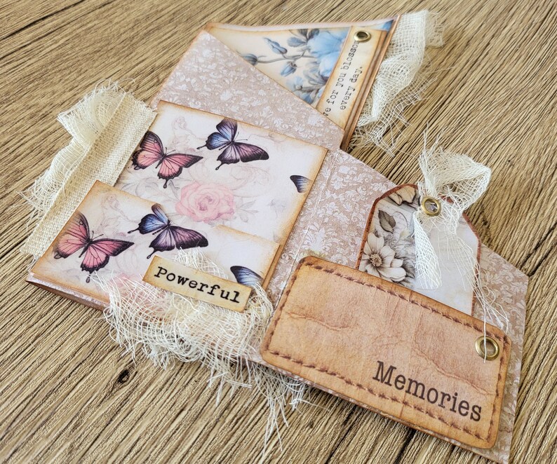 K&ouml;nnte beinhalten: Ein handgemachtes Scrapbook mit Vintage-&Auml;sthetik. Der Umschlag zeigt ein Blumenmuster mit Schmetterlingen und den Worten "be for you blossom every day". Die Innenseiten haben eine Vielzahl von dekorativen Elementen, darunter Spitze, Stoff und Papier. Das Scrapbook ist mit den Worten "Powerful" und "Memories" verziert.