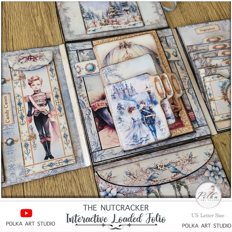 Op de afbeelding: Een meerlaags papierkunstig folio met een winterthema. De voorkant heeft een blauwe en witte illustratie van een kasteel en een stel in winterkleding. De titel "The Nutcracker Interactive Loaded Folio" staat op de voorkant gedrukt. Het folio is ontworpen om te gebruiken als een scrapbook of dagboek.