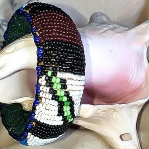 May include: A beaded bracelet with a colorful geometric pattern in shades of black, white, brown, blue, and green.