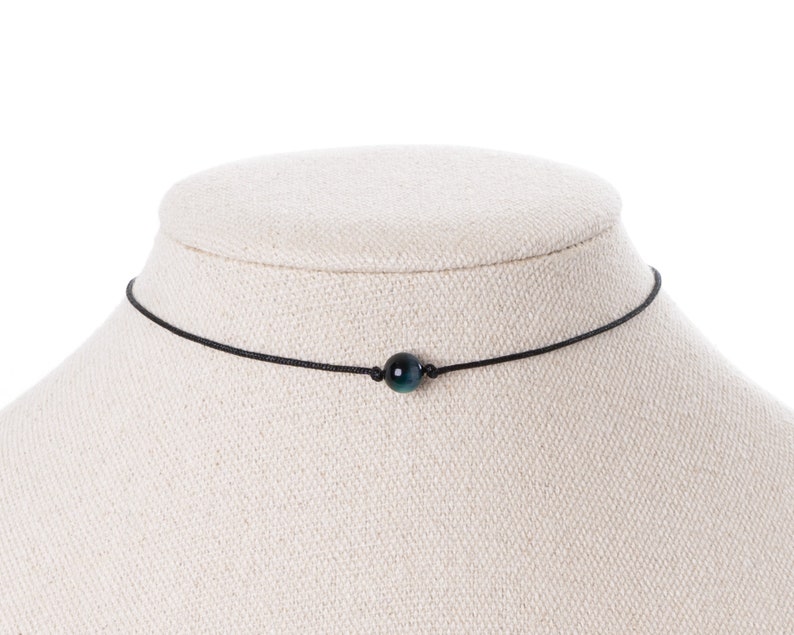 May include: A black choker necklace with a single dark blue and green gemstone bead.