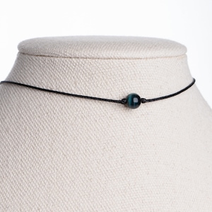 May include: A simple black cord necklace with a single dark blue and green tiger's eye bead.