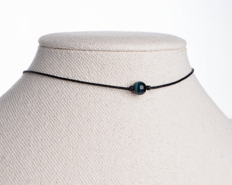May include: A simple black cord necklace with a single dark blue and green tiger's eye bead.