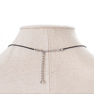 May include: A black cord necklace with a silver chain extender. The necklace is displayed on a fabric-covered mannequin bust.