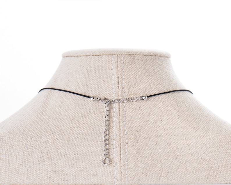 May include: A black cord necklace with a silver chain extender. The necklace is displayed on a fabric-covered mannequin bust.