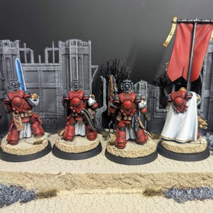 May include: Four red and white painted miniature figures of space marines standing on circular bases. The figures are holding weapons and are wearing armor. One figure is holding a banner with a red and white design.
