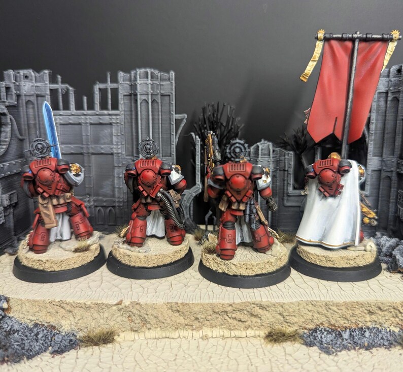 May include: Four red and white painted miniature figures of space marines standing on circular bases. The figures are holding weapons and are wearing armor. One figure is holding a banner with a red and white design.