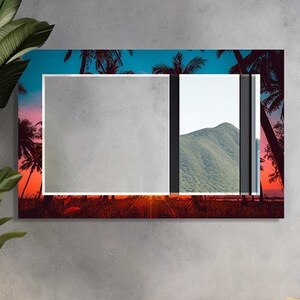 May include: A rectangular wall art piece featuring a sunset scene with palm trees. The artwork has a vibrant color palette of orange, red, and blue. The piece is mounted on a gray wall in a modern living room setting.