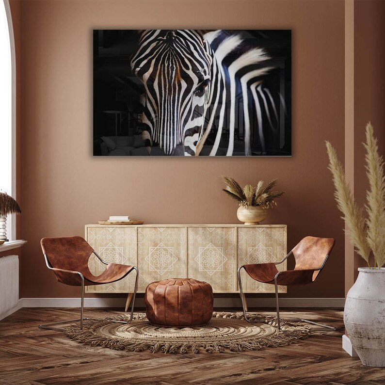 May include: A black and white zebra portrait in a modern living room setting with two brown leather chairs, a wooden cabinet, and a woven rug.