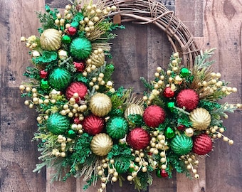 May include: A festive Christmas wreath with a woven grapevine base. The wreath is adorned with green, red, and gold ornaments, berries, and sprigs of greenery. The wreath is a holiday decoration.