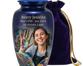 May include: A dark blue metal cremation urn with a matching lid, featuring a printed photograph of a smiling person with paint-covered hands. The text reads Avery Jenkins, Mar 1990 - Jun 2024, An Artistic Light. A purple velvet drawstring bag sits behind.