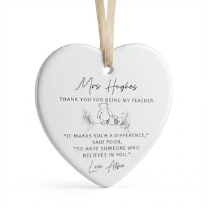 May include: A white heart-shaped ceramic ornament with a beige ribbon for hanging. The ornament features the text "Mrs Hughes, THANK YOU FOR BEING MY TEACHER" and a quote from Winnie the Pooh, along with the name "Love Alfie".