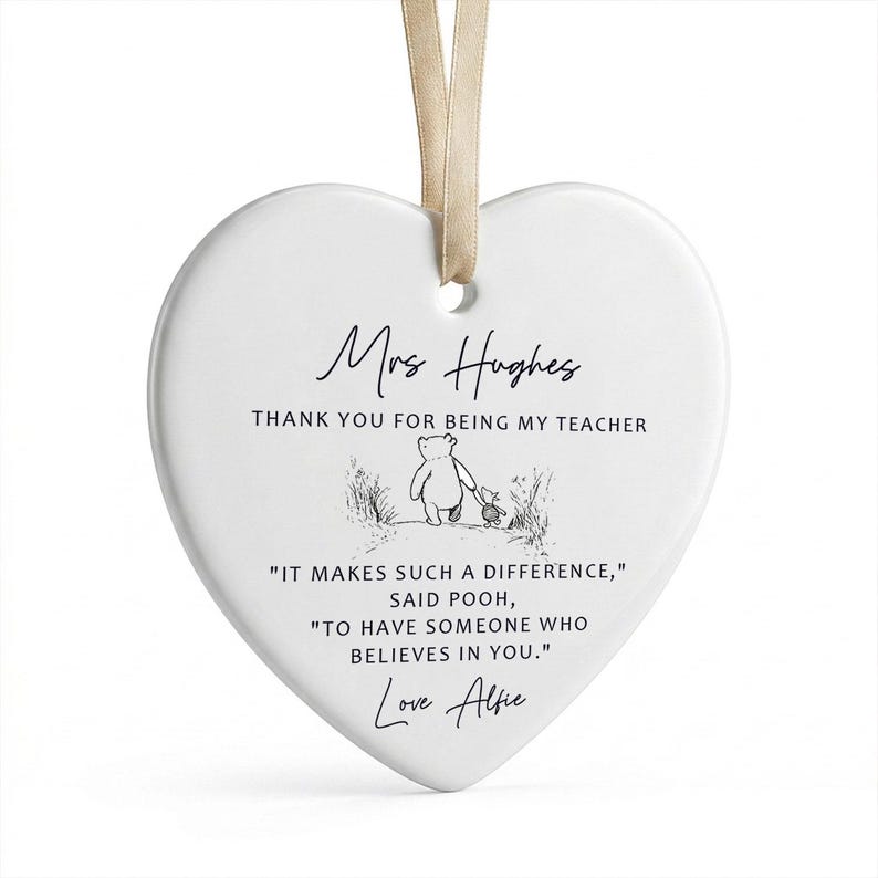 May include: A white heart-shaped ceramic ornament with a beige ribbon for hanging. The ornament features the text "Mrs Hughes, THANK YOU FOR BEING MY TEACHER" and a quote from Winnie the Pooh, along with the name "Love Alfie".