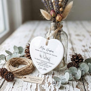 May include: A white heart-shaped ceramic plaque with a ribbon for hanging. The plaque has text that reads "Mrs. Hughes, Thank you for being my teacher." and a Winnie the Pooh illustration. A small tag reads "Handcrafted Ceramic."