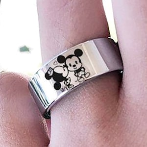 May include: A silver ring with a black and white image of Mickey Mouse and Minnie Mouse holding hands.