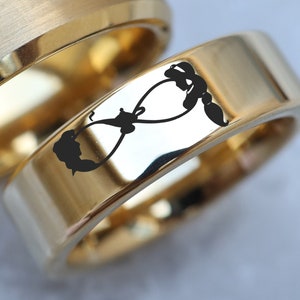 May include: Two gold wedding bands, one with a brushed finish and the other with a polished finish. The polished band has an infinity symbol engraved on it.