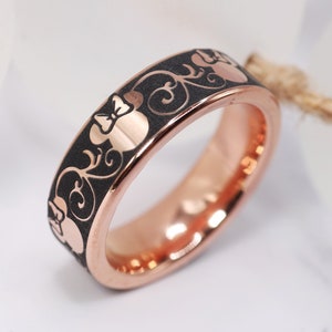 Op de afbeelding: Een ros&eacute;gouden ring met een zwarte emaille afwerking en een herhalend patroon van een cartoon muizenkop met een strik.