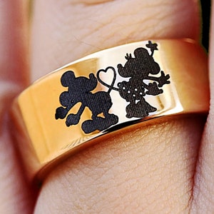 May include: A gold ring with a black silhouette of Mickey Mouse and Minnie Mouse holding hands with a heart between them.